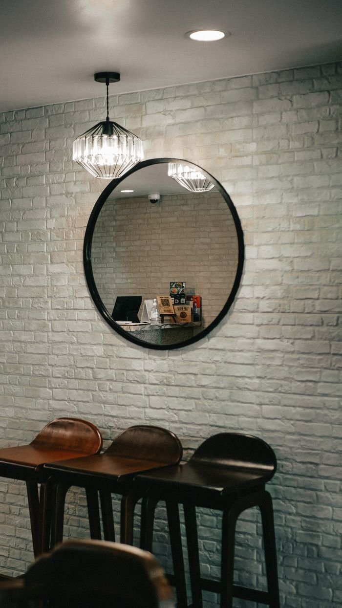 Elegant coffee shop interior featuring a round mirror on a white brick wall with stylish stools.