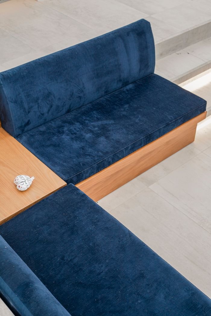 A high-angle shot of a minimalist blue sofa with a wooden frame in a sunlit living room.