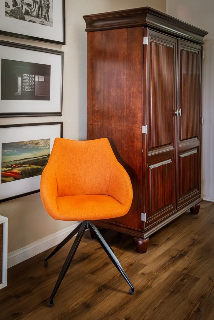 A vibrant orange chair complements a vintage armoire in a modern apartment setting.